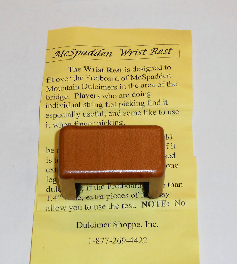 A brown Wrist Rest for Ginger Dulcimers, crafted from walnut wood by McSpadden, sits atop a yellow instruction sheet for dulcimer players.