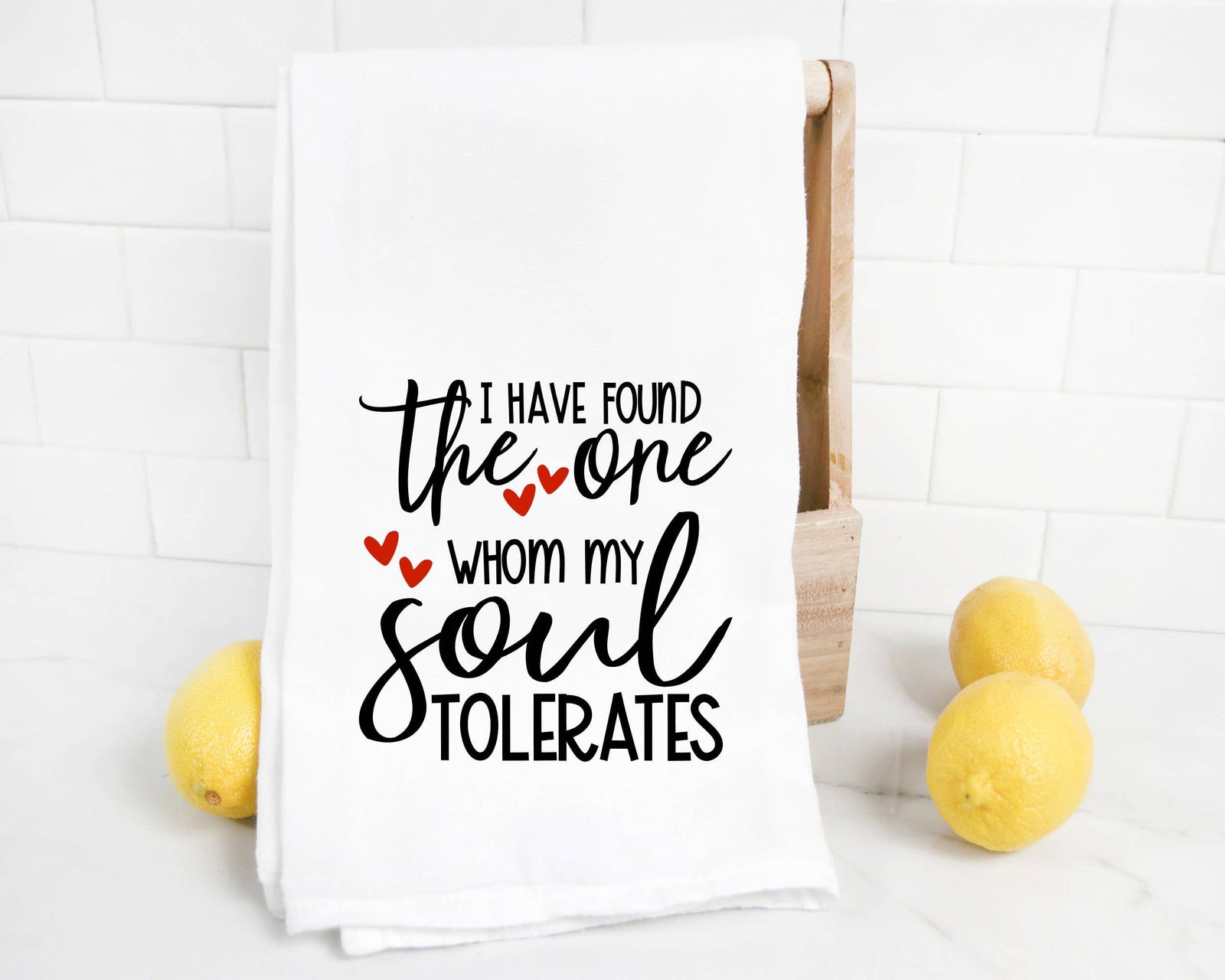 The discontinued Soul Tolerates Tea Towel features black and red text, "I have found the one whom my soul tolerates," making it a quirky anniversary gift or playful love towel for your home. Displayed beside lemons on a white countertop.