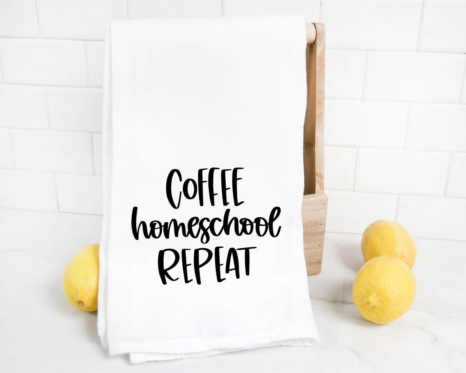 The discontinued Coffee Homeschool Repeat Tea Towel features black script on white and is shown beside lemons—an ideal back-to-school gift for teachers or homeschoolers.